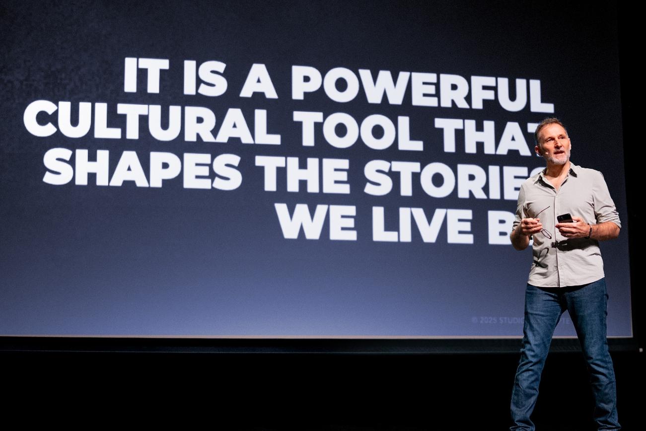 Patrick Larsen, production designer, on stage during a keynote — design as a powerful cultural tool that shapes the stories we live by.