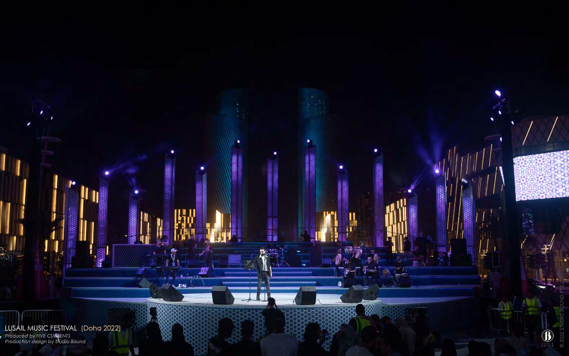 Wide hero view of the Darb Lusail stage in turquoise and violet, with patterned media walls flanking the boulevard.