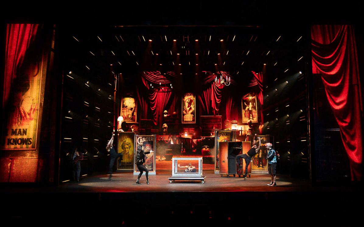 The parlour scene in motion — the ensemble inside the show's nineteenth-century magic-hall world, framed by the touring shell. Production design by Patrick Larsen, Studio Bound.