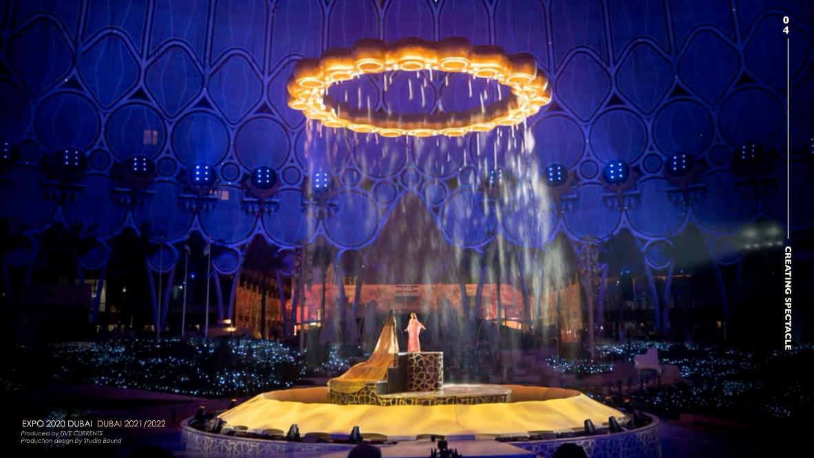 The signature moment in performance — the illuminated ring suspended above the central mound as Hope is revealed in the garden, dome dressed in deep blue projection. Production design by Studio Bound.