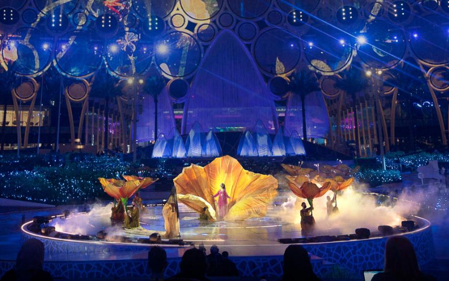 The golden bloom — petals opening on the central disc with a soloist at its heart, Al Wasl carrying the moment for both the live audience and the broadcast camera. Production design by Studio Bound.