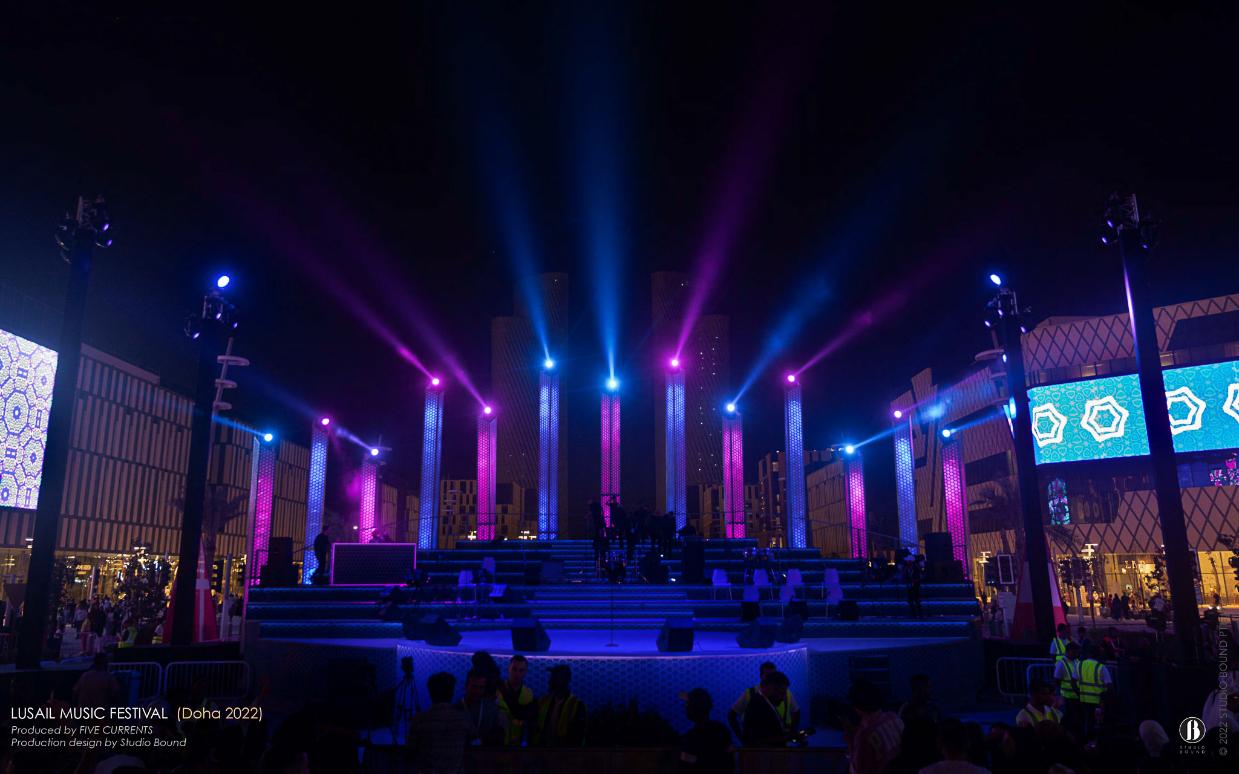 Empty Darb Lusail boulevard stage at dusk with magenta and cyan beams piercing through a forest of perforated columns.