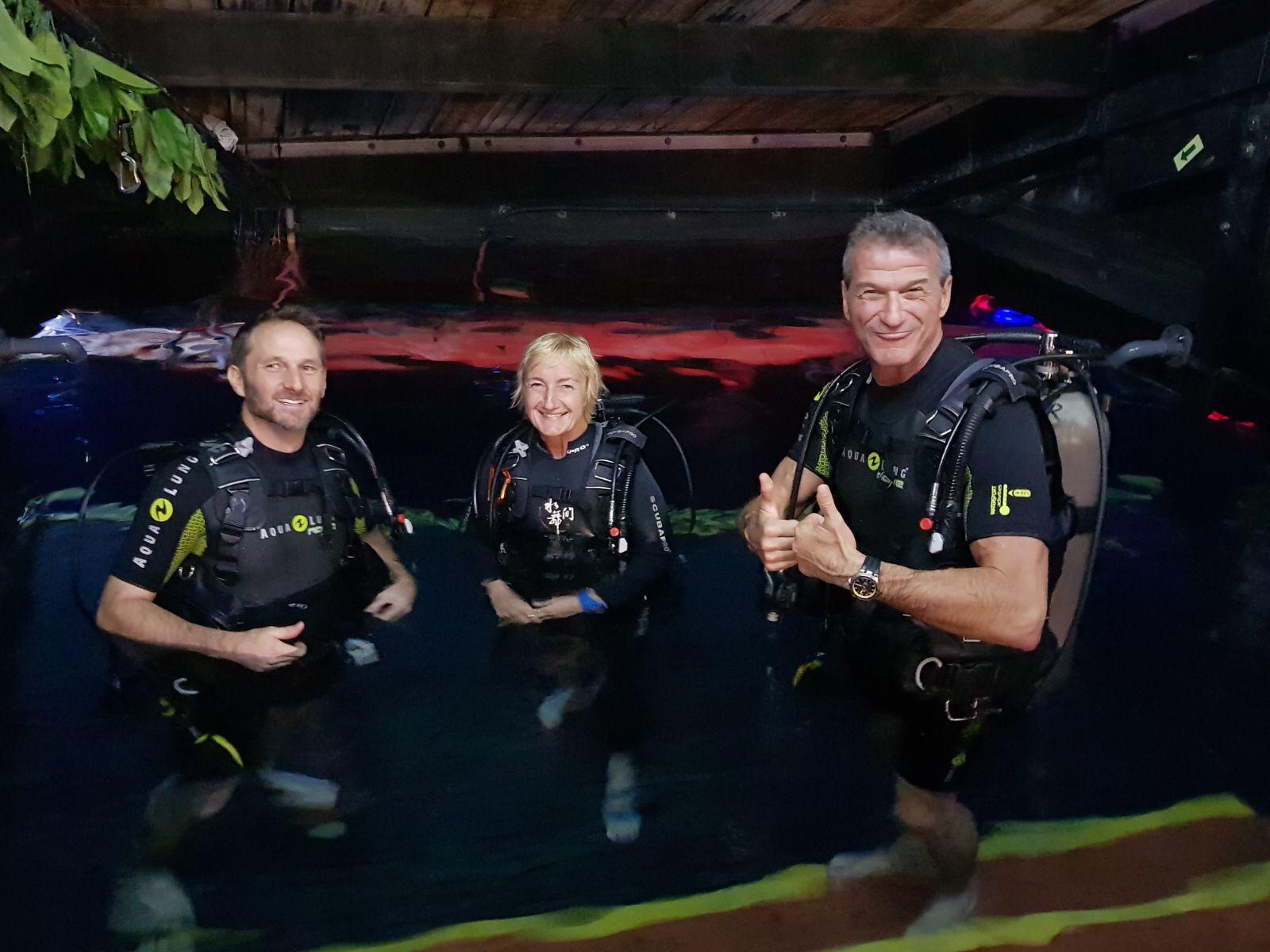 Patrick Larsen in dive gear alongside two colleagues, standing in a backstage water tank ready to dive.