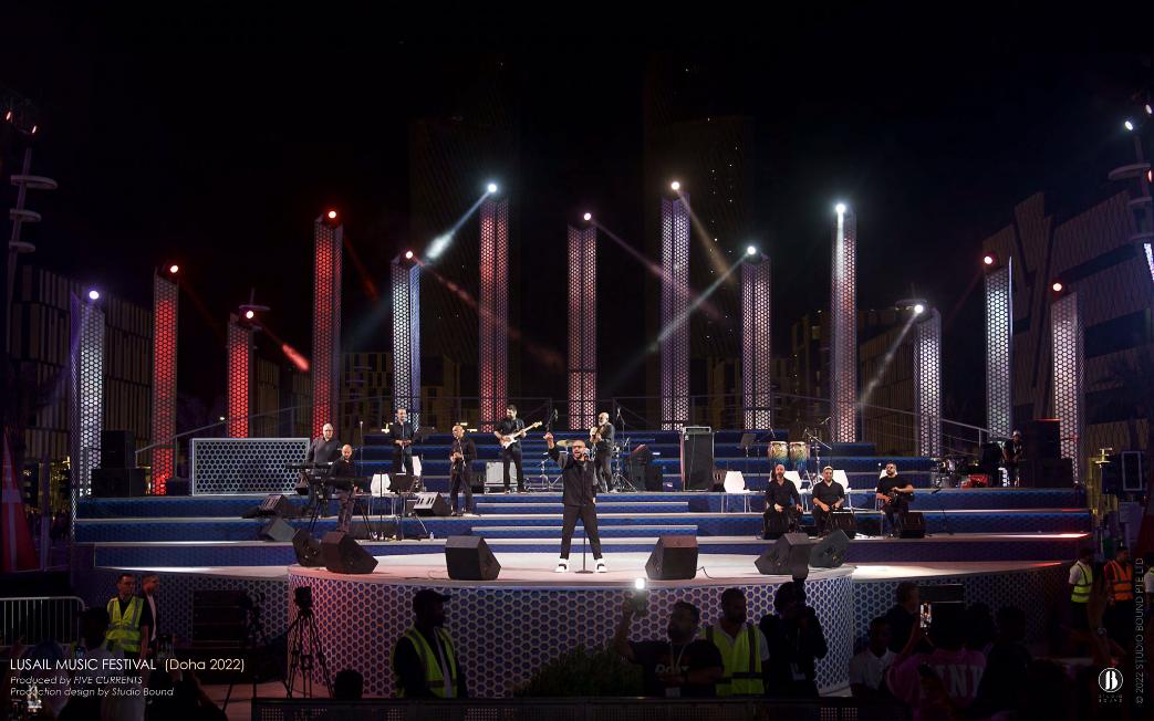 Wide telephoto view of the Darb Lusail stage with the band in silhouette, columns in red and white against the Lusail towers.