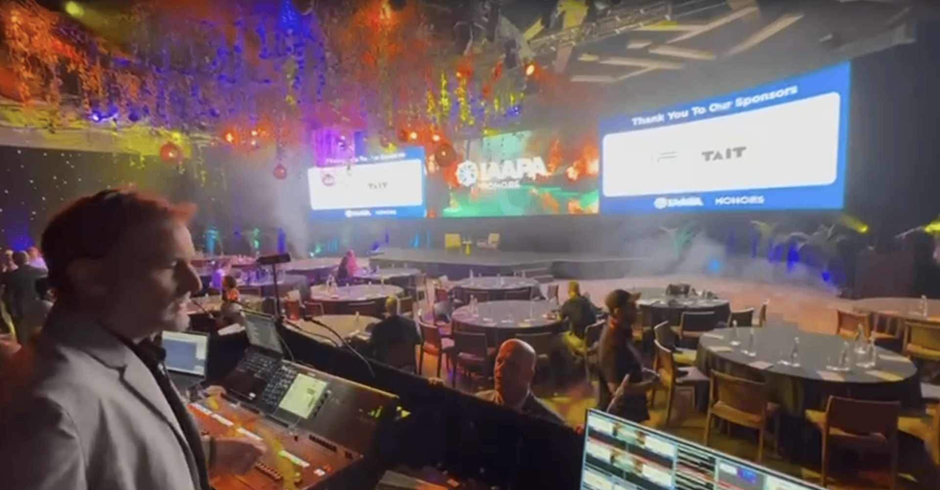 Patrick Larsen at the front-of-house control position during the IAAPA Honours show, with the stage and sponsor screens lit in the background.