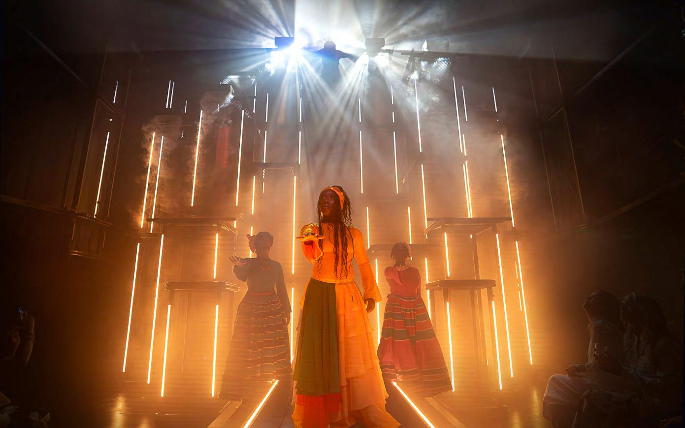 The same cathedral re-lit in amber for a quieter passage — proof that one set of architecture, well drawn, can carry several different rooms across the journey. Scenic design by Studio Bound.