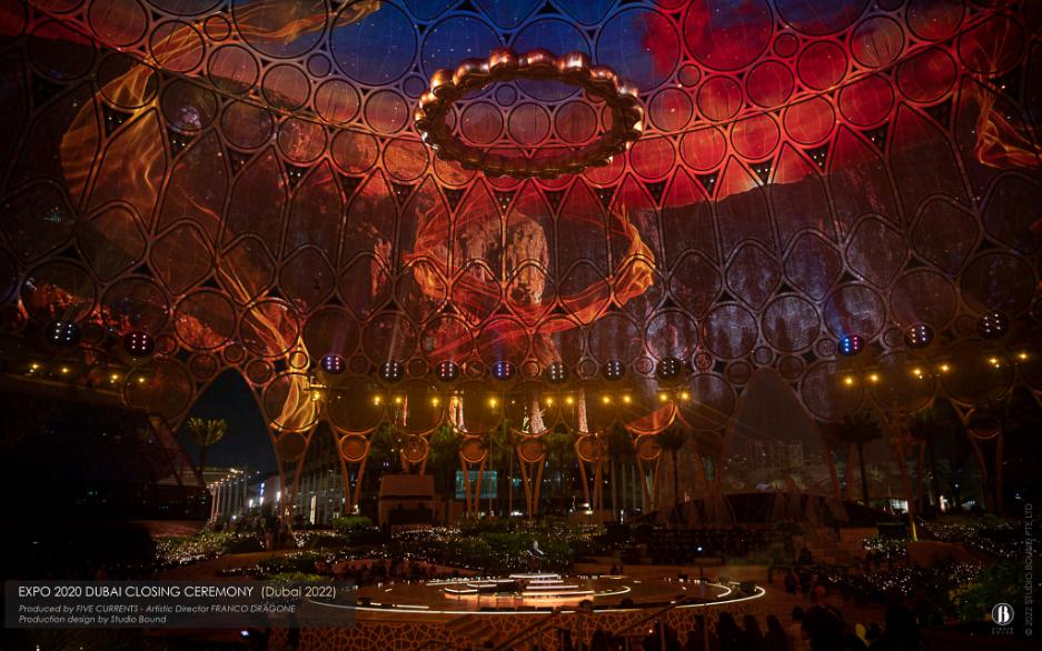 Closing Ceremony, March 2022 — the dome redrawn in red, the Expo Ring returning overhead to bracket the six months in between with a single piece of architecture. Production design by Studio Bound.