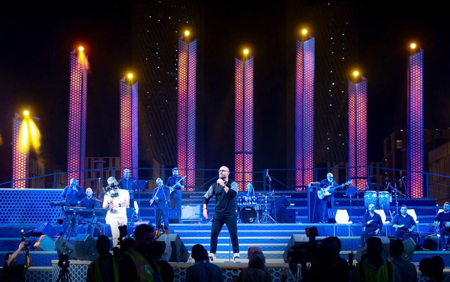 Closer view of the Darb Lusail stage in purple and amber, full band visible on the stepped riser behind the soloist.