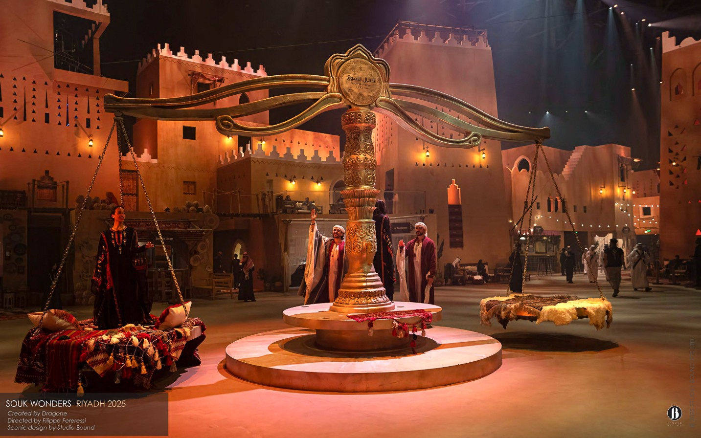 The Mizan — a monumental sculptural balance at the heart of the souk, its swinging platforms used as performance pods carrying singers, dancers and storytellers above the crowd. Scenic design by Studio Bound.