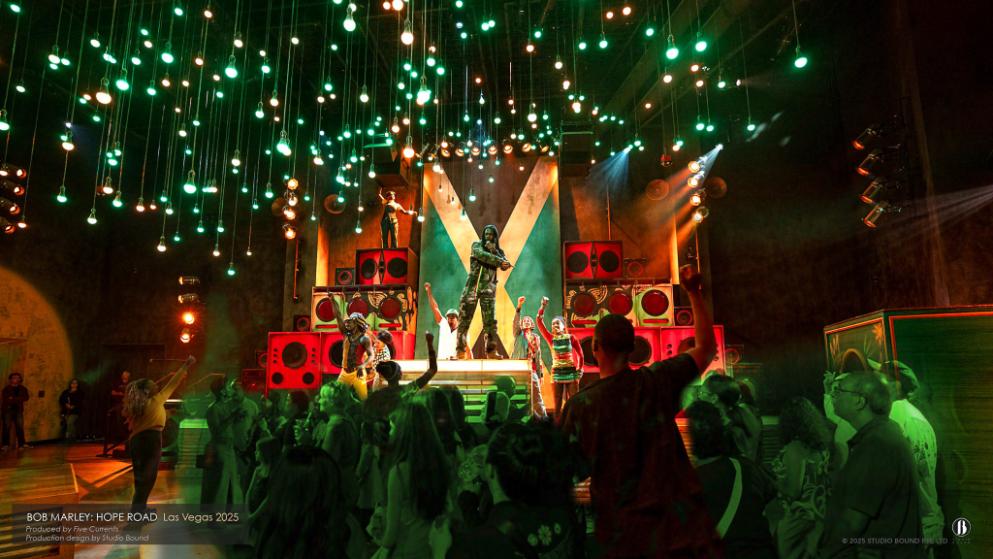 The same dancehall opened up for the full band — a green Jamaican cross painted across the back wall, hundreds of warm bulbs hung as a low ceiling of light, guests pulled in on every side. Production design by Patrick Larsen, Studio Bound.