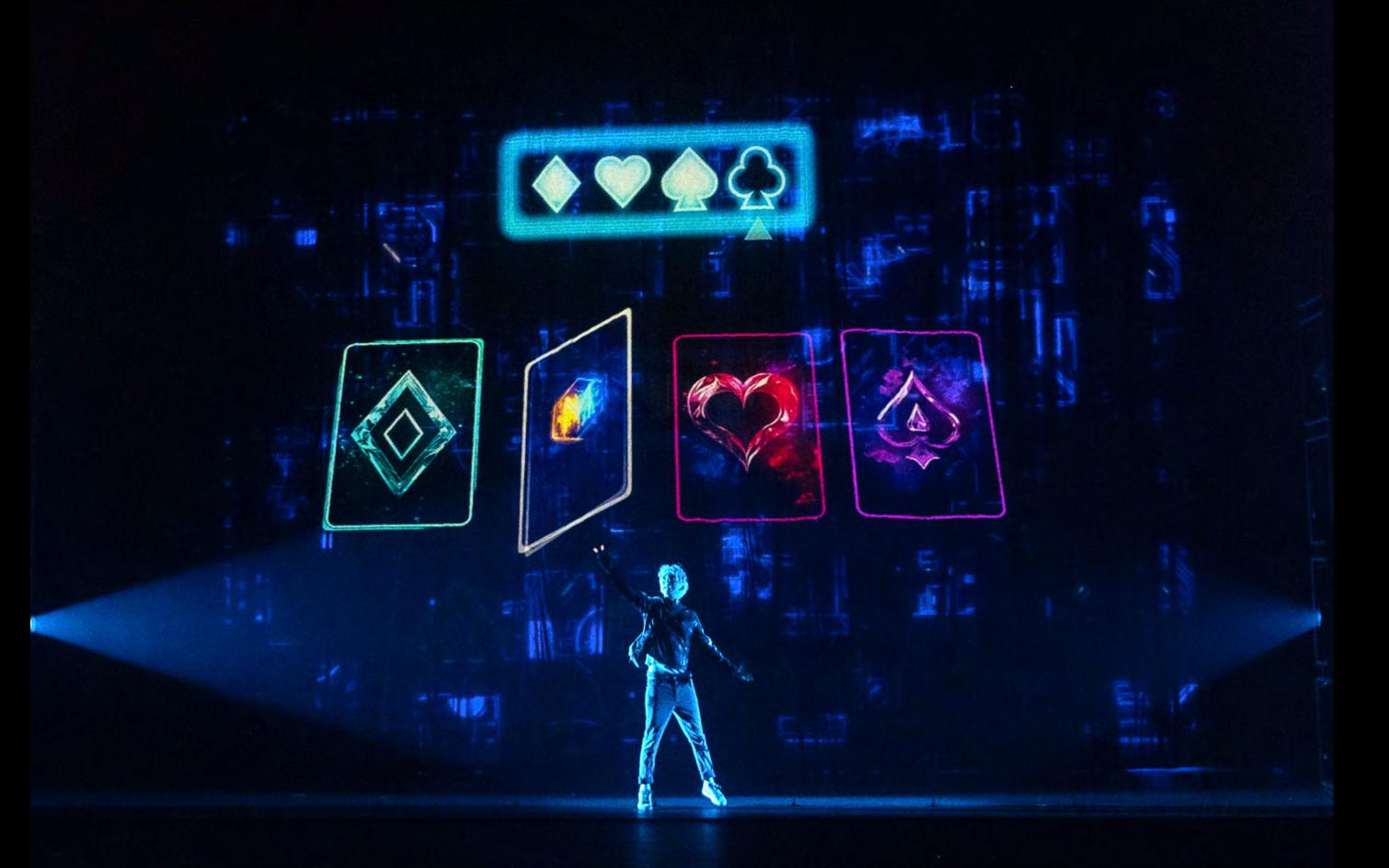 A "pick a card" sequence rendered as oversized neon playing cards on screen — the audience choosing in real time from their phones. Production design by Patrick Larsen, Studio Bound.