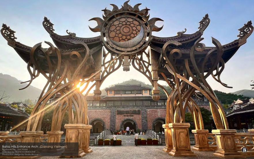The completed Base Camp arch at sunset — sun motif backlit, columns silhouetted, the design holding its own against the mountain. Production design by Patrick Larsen, Studio Bound.