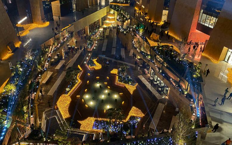 Aerial view of the VIA Riyadh courtyard at night, paths and plazas lined with thousands of warm candles weaving between buildings.
